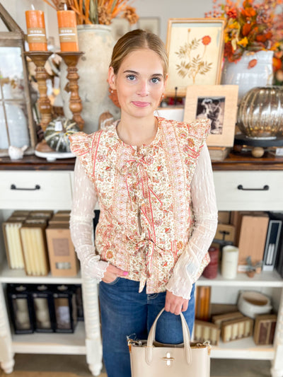 cream, pink, and red floral vest with bow tie closure down the front with ruffles on the sleeve and a cream lace laying tee underneath 