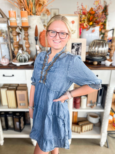 denim dress with brown stitching and smocking at the neckline and ruffle hem at the bottom 